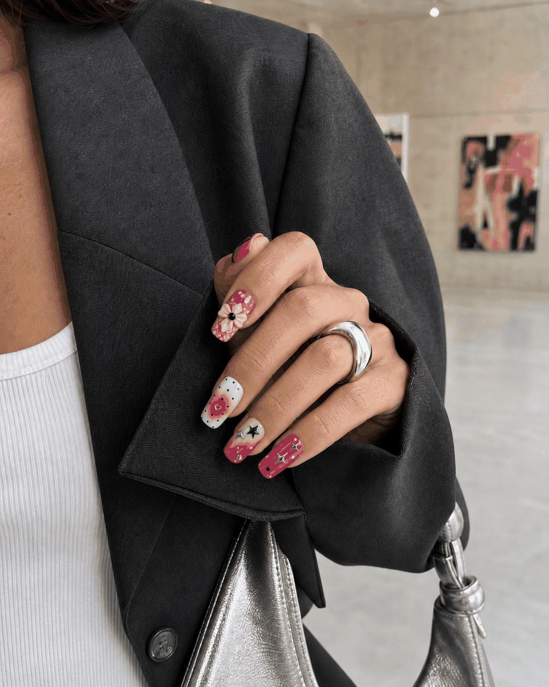 Woman in a charcoal blazer wearing pink graphic press-on nails at a gallery